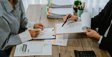 Two businesswomen in suits sit in a meeting. On the table are tablets, laptops, and graph documents.