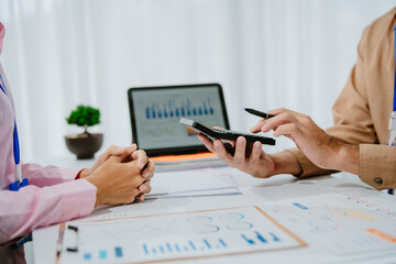 Two Asian businesspeople smiling and engaging in a strategic discussion while using a laptop in a modern office environment