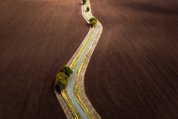 Top down daylight view of freshly ploughed and harvested agricultural fields on a farm, winding road with green grass and trees during mid day sun.  Summer drone photograph copy space no people