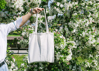 Woman hand holding eco bag. Female hold white canvas textille mesh zero waste shopper on city...