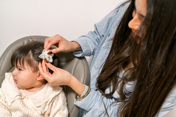 Fototapeta premium Mother putting a white flower hair clip on her baby girl's hair