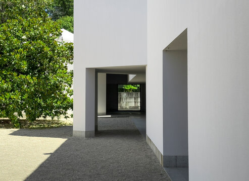 Minimalist white building with geometric passage and shadows next to a green tree in Serralves Park,