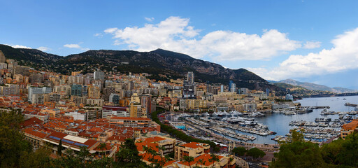 Elevated view of a Monaco cityscape with layered high-rises and red rooftops nestled in green hills.