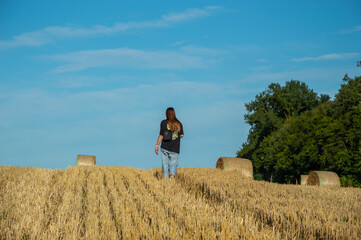 A woman strolls through sunlit fields, surrounded by rolled hay bales, enjoying the tranquility of...