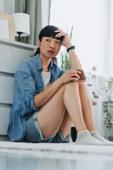 Depressed asian mature woman holding alcohol flask at home