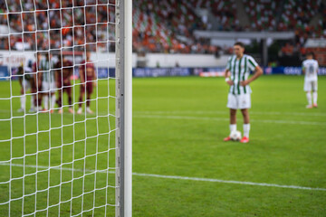 Detail of goal's post with net and football player during penalty kick in the background.