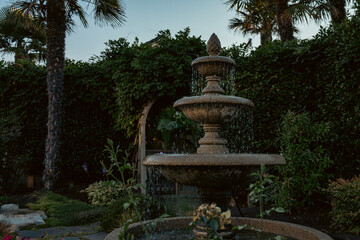 Dark and Moody Flowing and Splashing Fountain in a Quiet Botanical Garden during golden hour at dusk with palm trees and lush greenery in the background