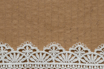 A piece of brown cardboard with white lace at the bottom as a background or texture for decoration,...