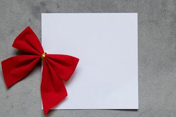 A white sheet of paper in the form of a card is located on a gray velour background and a red bow...