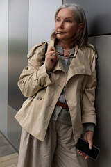 Stylish older woman poses elegantly near modern building in daytime