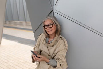 Stylish woman using smartphone while leaning against modern architecture in urban setting