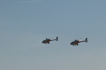 Two training helicopters flying in formation against blue sky.