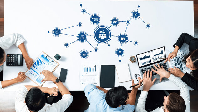 A diverse team collaborates at a modern office table surrounded by digital media and data visualizations, emphasizing effective project management and strategic communication. Amity - Powered by Adobe