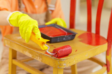 Painting wooden chair with red roller during DIY home renovation