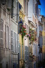 Fototapeta premium Vintage Marseille street with colorful shuttered windows and flower pots in historic Le Panier district on sunny day