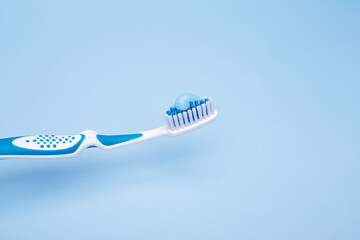 White and blue toothbrush with fresh blue gel toothpaste on bristles against pastel background