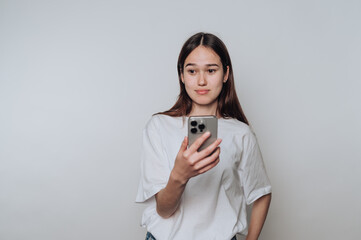 Young woman in white shirt using smartphone against plain background.