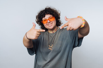 Person with curly hair wearing orange sunglasses and casual clothing, pointing with both hands,...