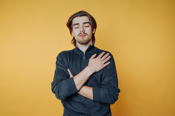 Fototapeta premium Young man with closed eyes and hand on chest against yellow background.