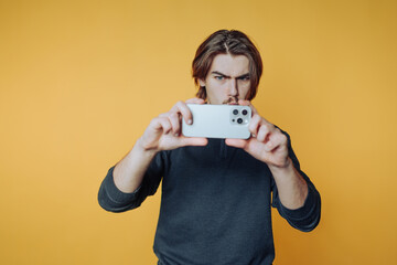 Man taking a selfie with a smartphone against a yellow background.