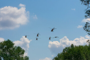 Five helicopters flying in V-formation against cloudy sky.