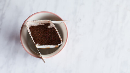 Drip bag in a ceramic cup on windowsill. Instant freshly brewed alternative filter drink in mug....