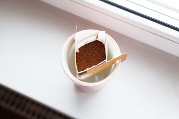 Drip bag in a ceramic cup on windowsill. Instant freshly brewed alternative filter drink in mug. Easy brew black coffee method for home, travel or office. cozy trendy lifestyle