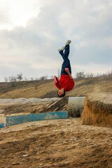 Young acrobat in red sweatshirt doing acrobatic trick with a turn in the air against the sky on the...