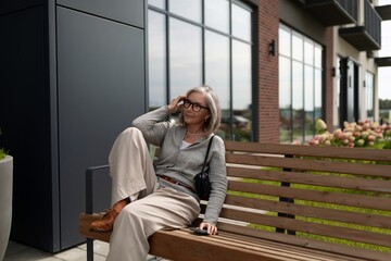 Mature woman relaxes on a bench outside a modern building during a cloudy day