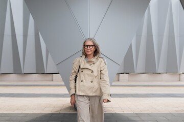 Woman walks confidently in stylish trench coat near modern architectural structure during daylight