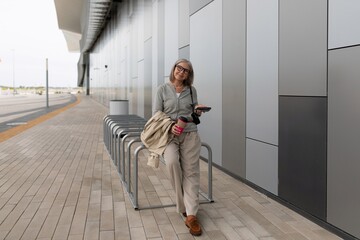 Young woman stands by bicycle rack in urban setting with coffee cup on cloudy day