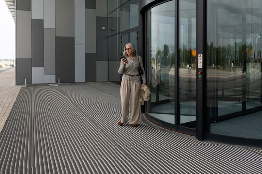 Older woman using smartphone while waiting outside modern building in urban area