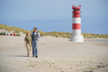 A loving couple strolls the sandy beach of Helgoland Düne with the iconic red-and-white lighthouse in the background, symbolizing romance, travel, and coastal lifestyle.