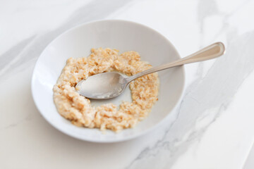 Creamy oatmeal with spoon in white bowl on marble surface