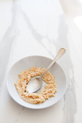Half-eaten bowl of oatmeal on marble table with spoon