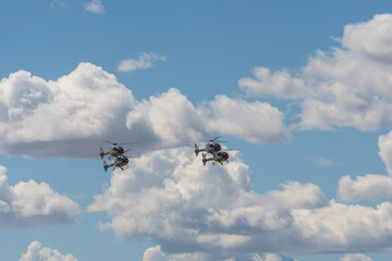 Two helicopters flying side by side against cloudy sky.