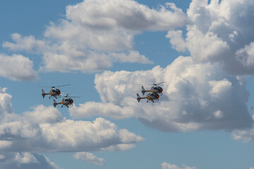 Helicopter squadron flying in open formation under cloudy sky.