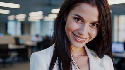 Attractive businesswoman stands in a bustling office environment, her warm smile and confident demeanor radiating professionalism and success