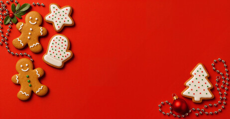 Top view of a wide red background with Christmas themed background with gingerbread cookies decorated with white icing.
