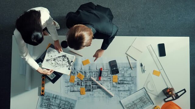 Time lapse of skilled project manager holding project plan and explain house design to architect engineer at meeting table with equipment, ruler, safety helmet and laptop scatter around. Alimentation.