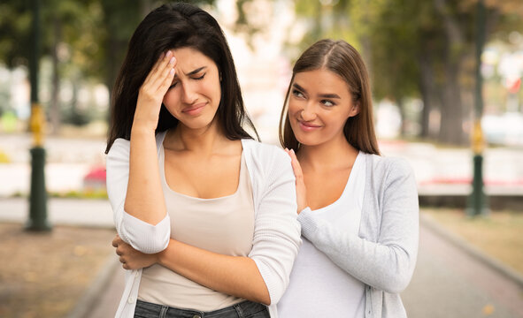 Fake Friendship Concept. Gloating Girl Rejoicing At The Misfortune Of Crying Female Friend Standing Outdoors.