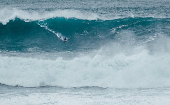 Lonely surfer on Huge Atlantic ocean wave during international surfers challenge at Praia do Norte in Nazare, Farol da Nazaré, Portugal where Guinness World Record for the highest surfing was set - Powered by Adobe