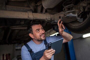 Mechanic inspecting car chassis using digital tablet in auto repair shop