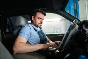 Car mechanic using laptop for diagnostics inside vehicle in auto repair shop