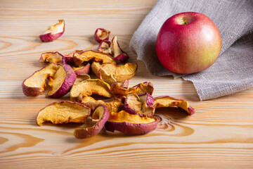 Red apple and dried apple slices on a wooden surface next to a linen napkin. The theme of natural...