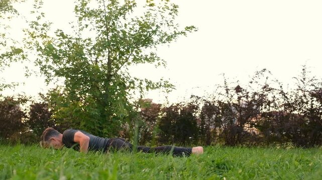 Mature man practicing yoga doing plank and Upward-Facing Dog Pose on green grass in park outdoors