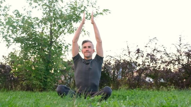 Man practicing yoga sitting in lotus pose on green grass in park outdoors