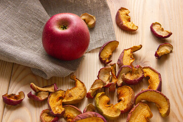 Red apple and dried apple slices on a wooden surface with a cloth napkin. Autumn theme, homemade preparations, farm food, natural products and comfort.