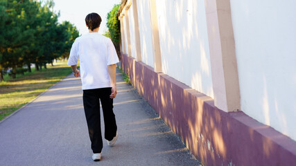 Young person walking along a tree-lined path in a sunny park during late afternoon hours
