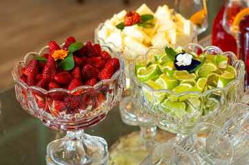 Glass bowls filled with fresh strawberries, pineapple cubes, and lime wedges, elegant fruit display for cocktails and catering events